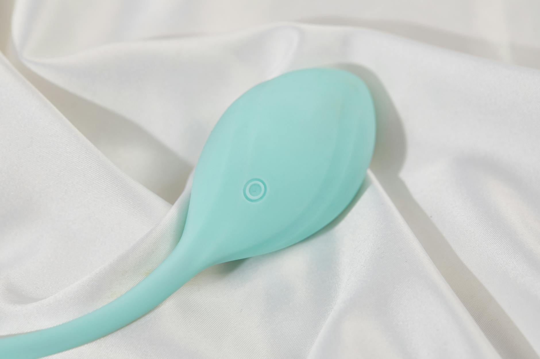 A sleek teal vibrator on smooth white silk fabric