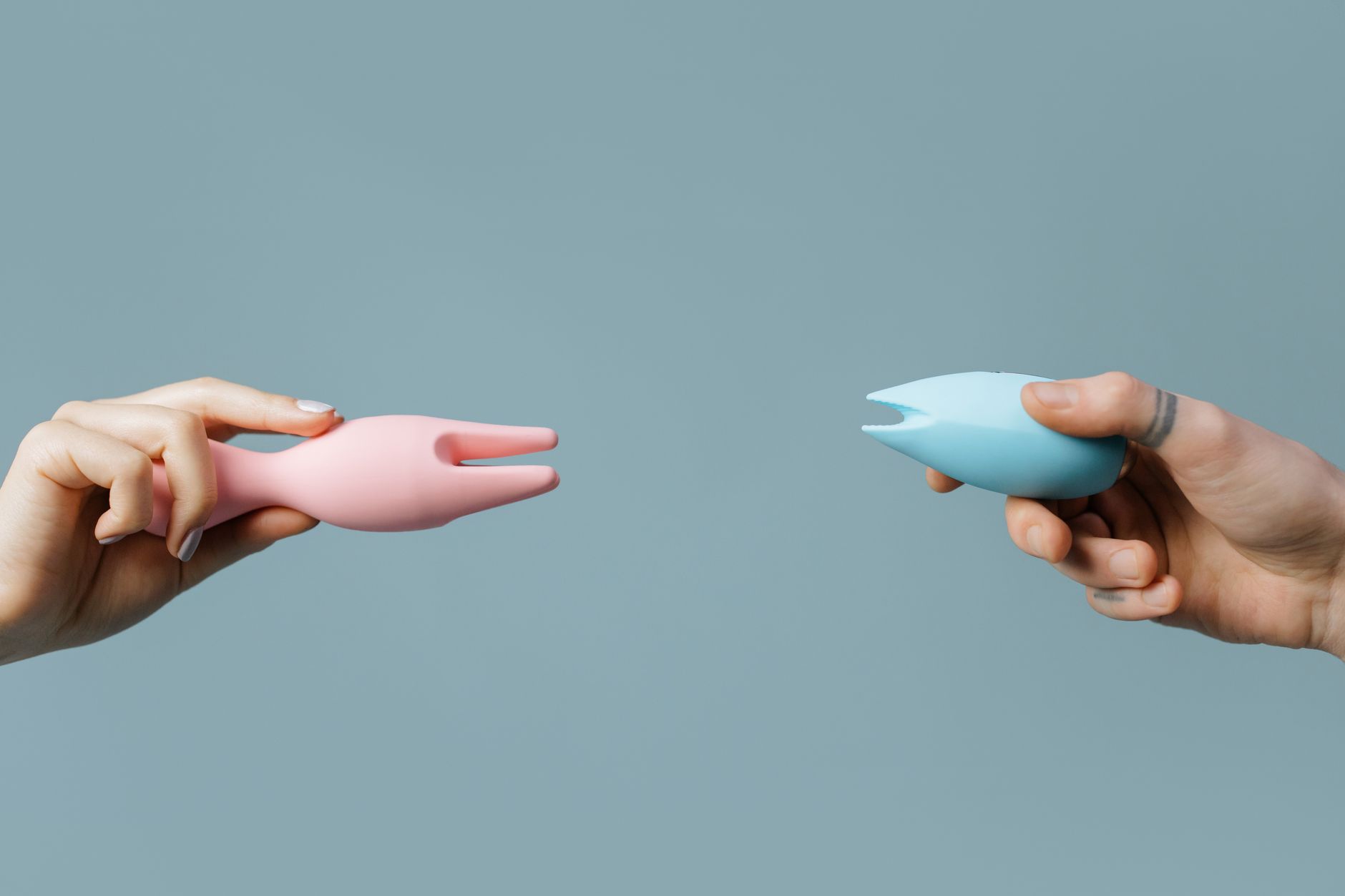 Woman holding pink and blue clitoral vibrators with calm expression